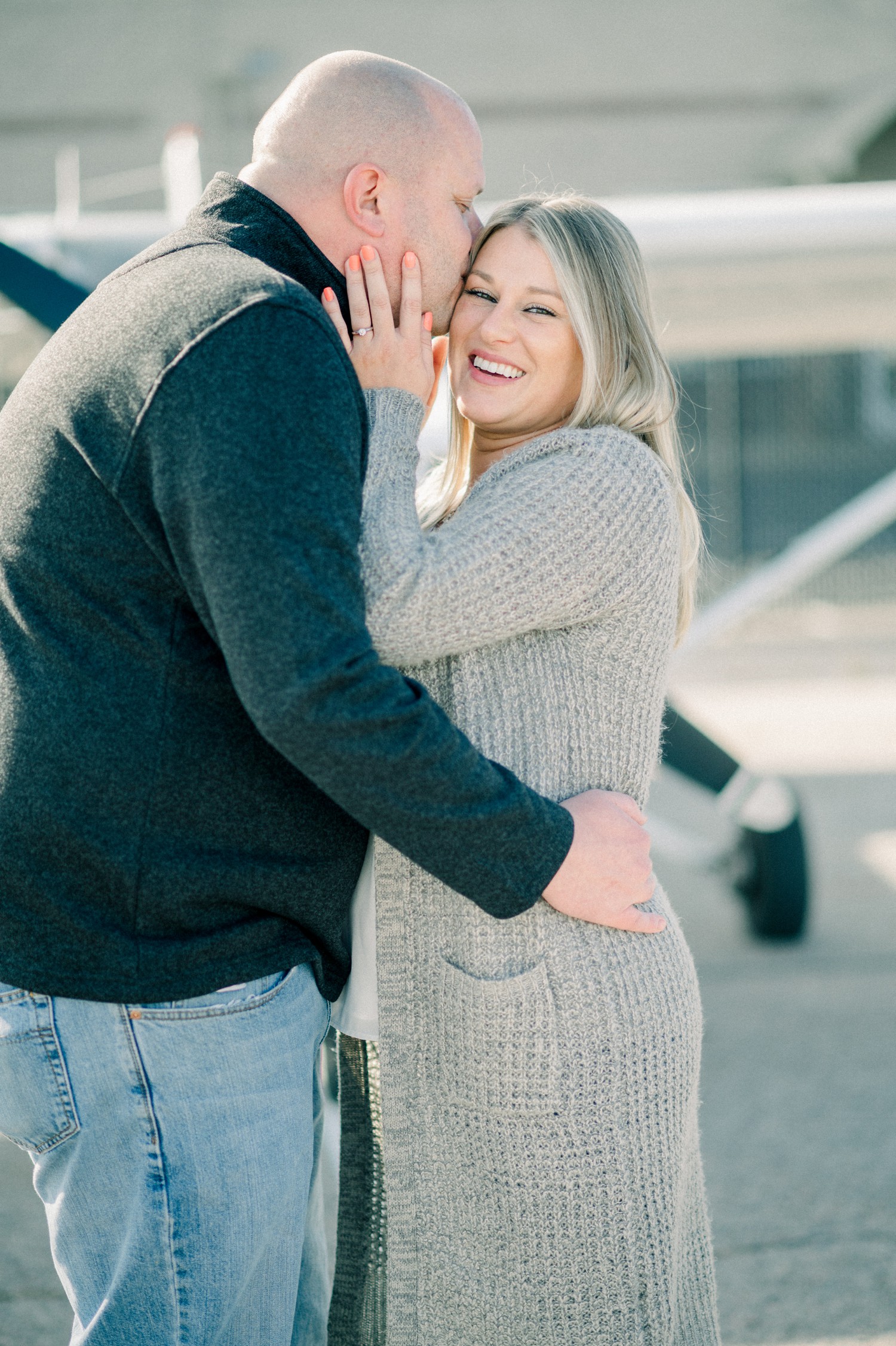 Guy kissing girl for engagement photos at airport.